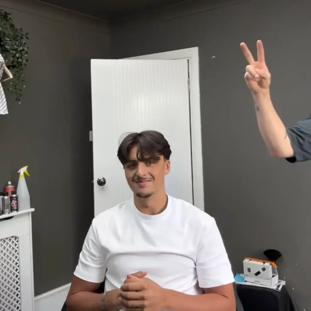 A client smiling after a fresh cut, with a peace sign from the barber